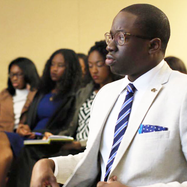 photo - young man in classroom setting, very well dressed in white suit, listening intently.