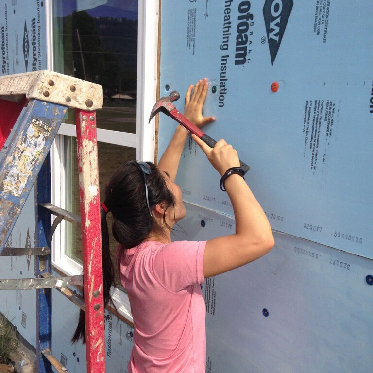 photo - young woman hammering on the side of a house under construction