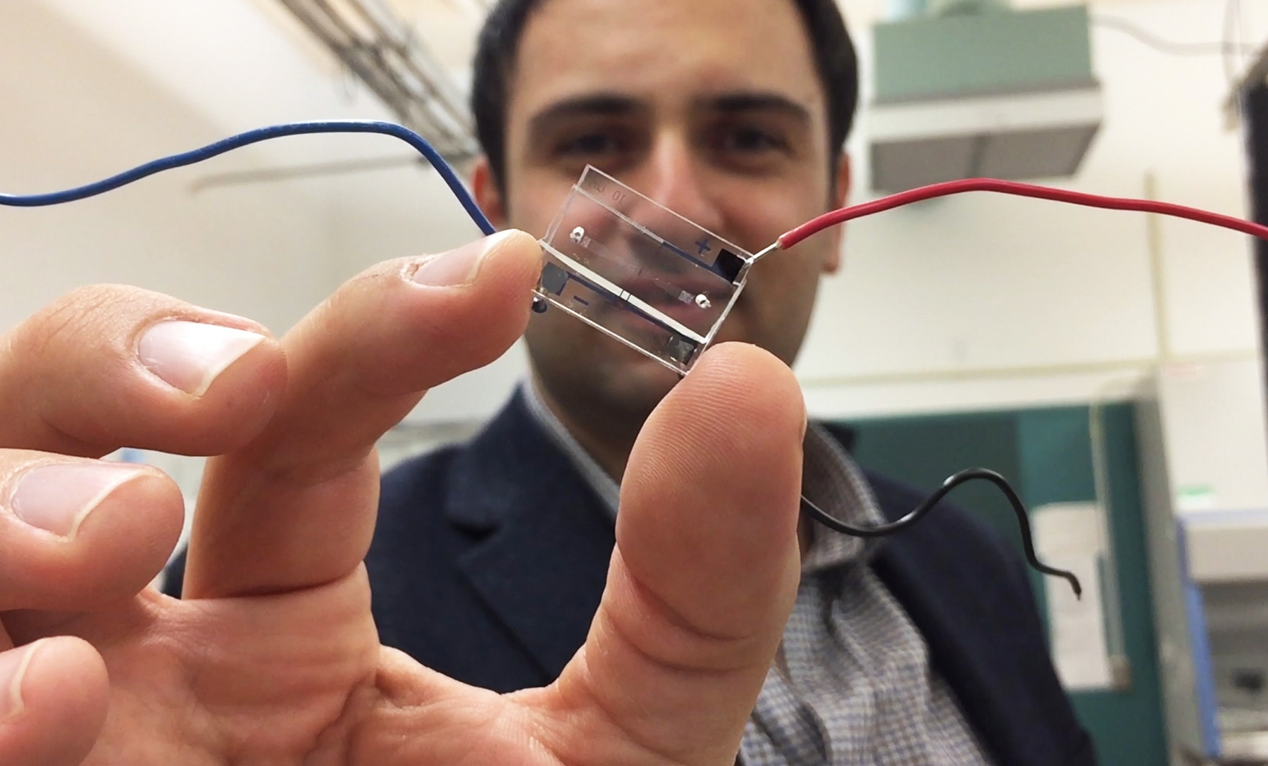Fatih Sarioglu, an assistant professor in Georgia Tech’s School of Electrical and Computer Engineering, holds a hybrid microfluidic chip that uses a simple circuit pattern to assign a unique seven-bit digital identification number to each cell passing through the channels. (Credit: John Toon, Georgia Tech)