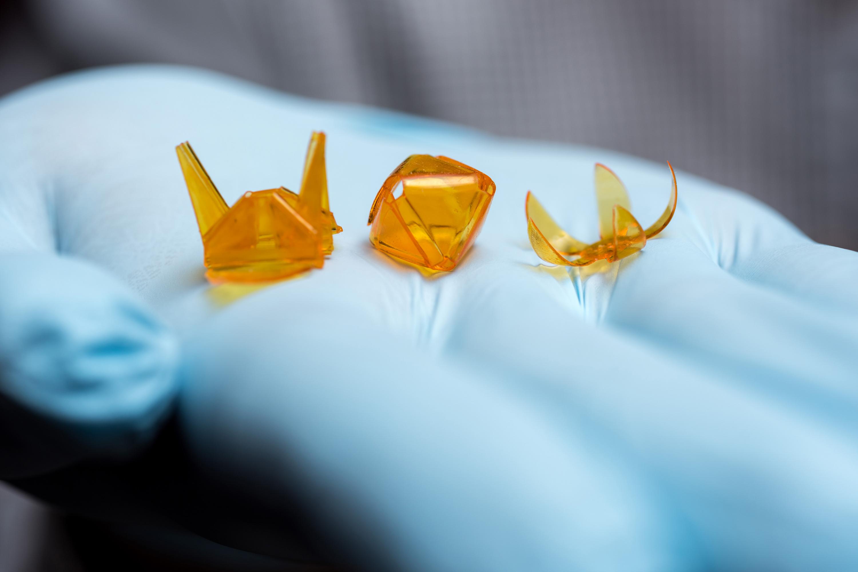 A new technique for producing self-folding three-dimensional origami structures from photo-curable liquid polymer materials created these tiny samples, held in a hand for size comparison. (Credit: Rob Felt, Georgia Tech)