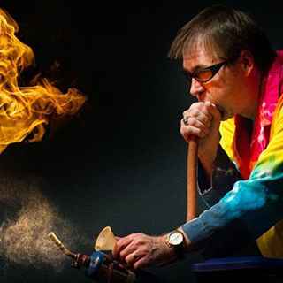 A man blowing through a hose and igniting flames.