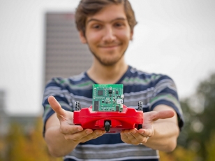 A computing student smiling and holding an electronic prototype of an invention