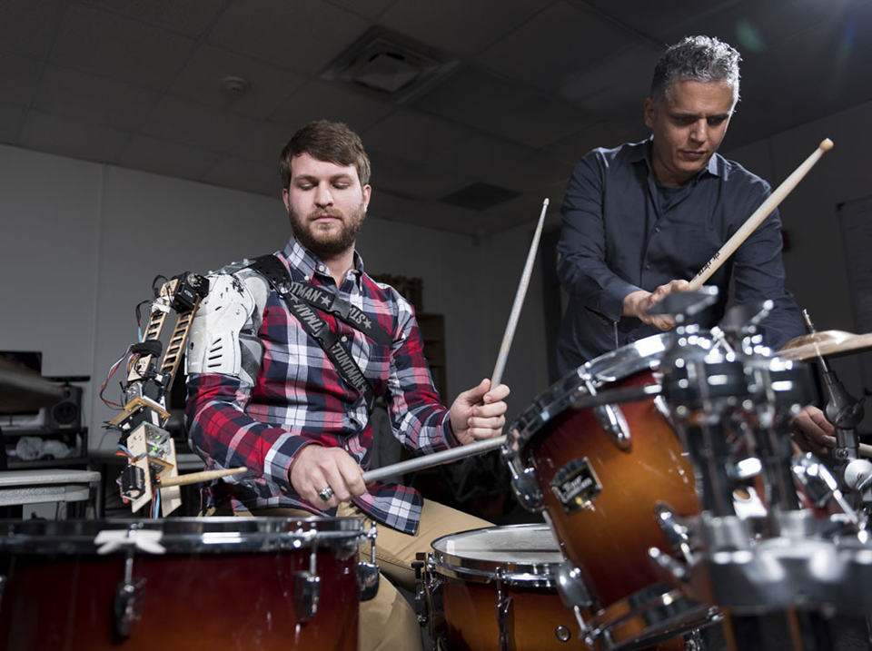 A drummer wearing a robotic arm plays with Professor Gil Weinberg