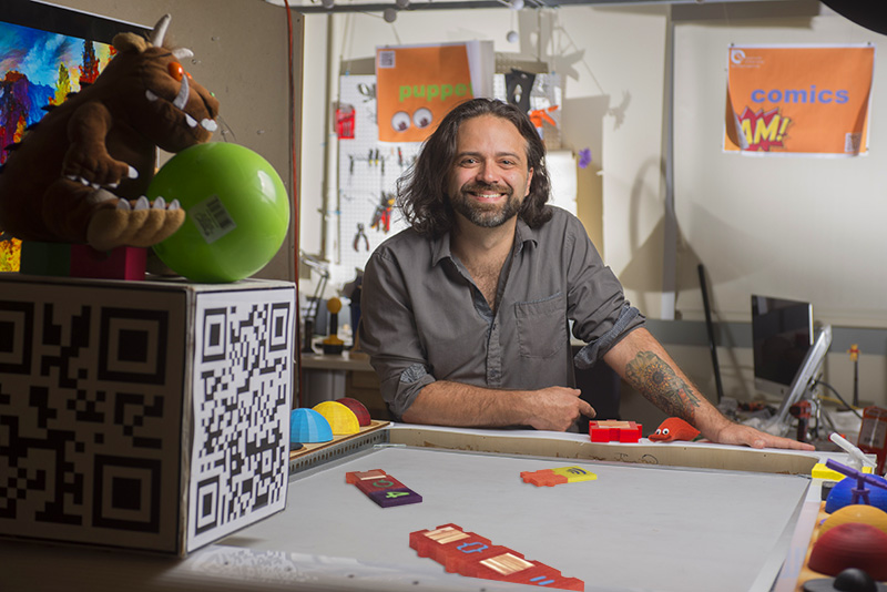 A portrait of Brian Magerko in his lab surrounded by colorful interactive projects