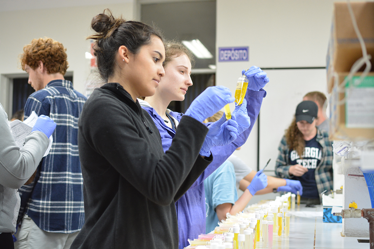 Two GT students in a lab in Bolivia hold up bags with that is yellow-colored