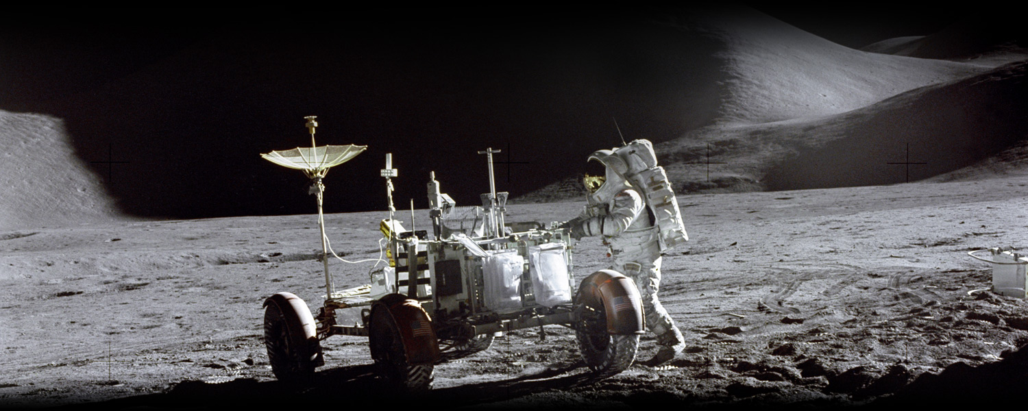 Astronaut James B. Irwin working on the Lunar Roving Vehicle on the moon's surface with a mountain in the background