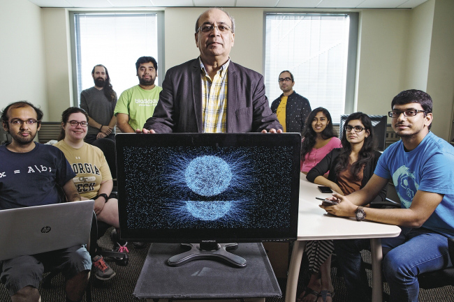 Ashok Goel and his students surrounding a computer with an abstract, interesting graphic displayed