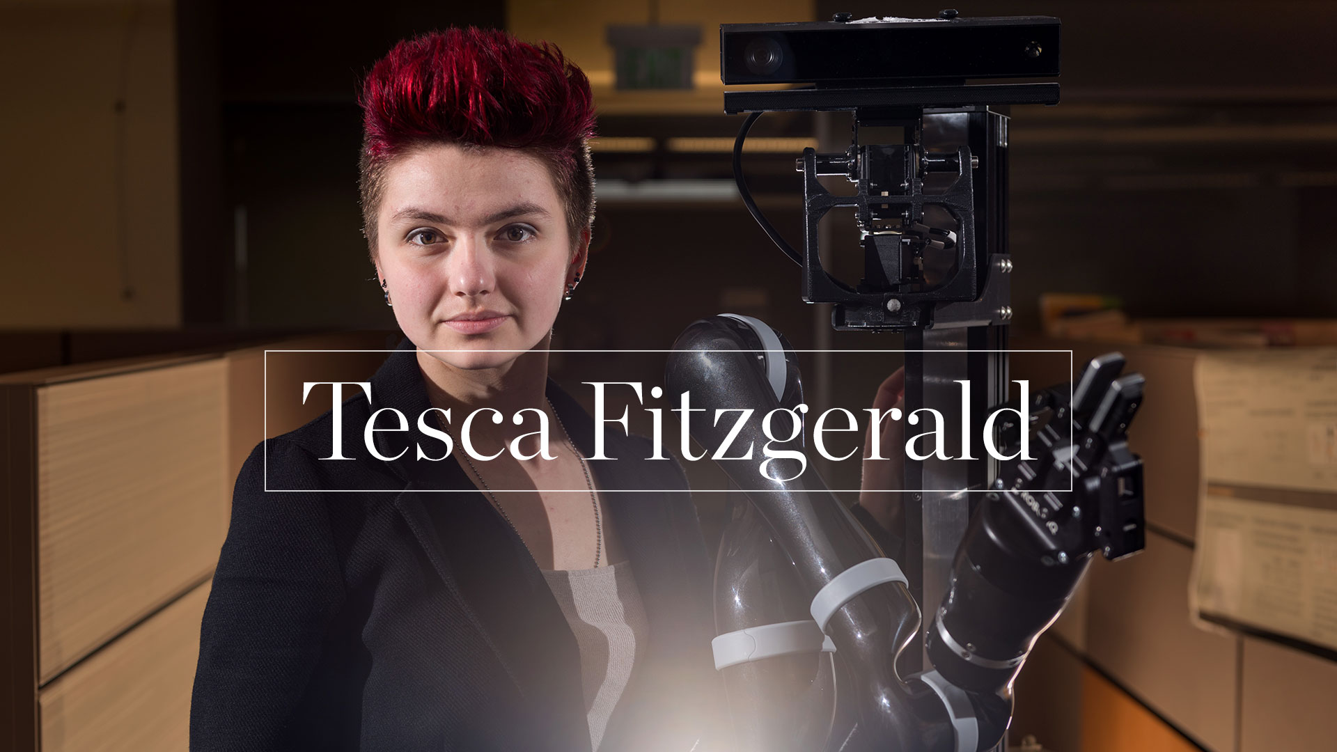 photo -  Tesca Fitzgerald standing with large robot in dark office setting 