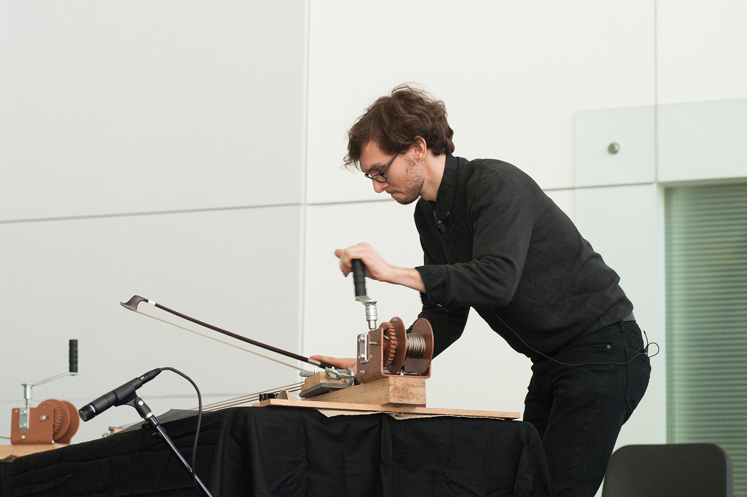Man playing a large instrument that has strings and a winch on one end; the man uses a bow to draw across the instrument