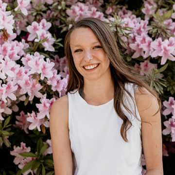 Nicole Shuster in a garden with pink flowers behind her