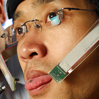 A graduate student demonstrates the headgear of the tongue drive wheelchair. A small magnet on his tongue allows him to control a mouse which moves the wheelchair.