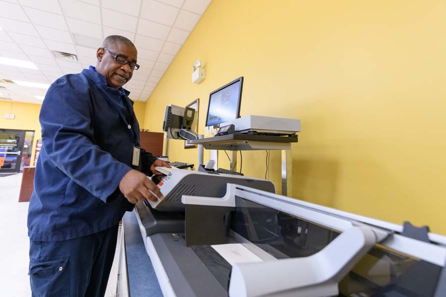 Postal Services lead and courier Rick Smith sends a stack of letters through the postage machine.