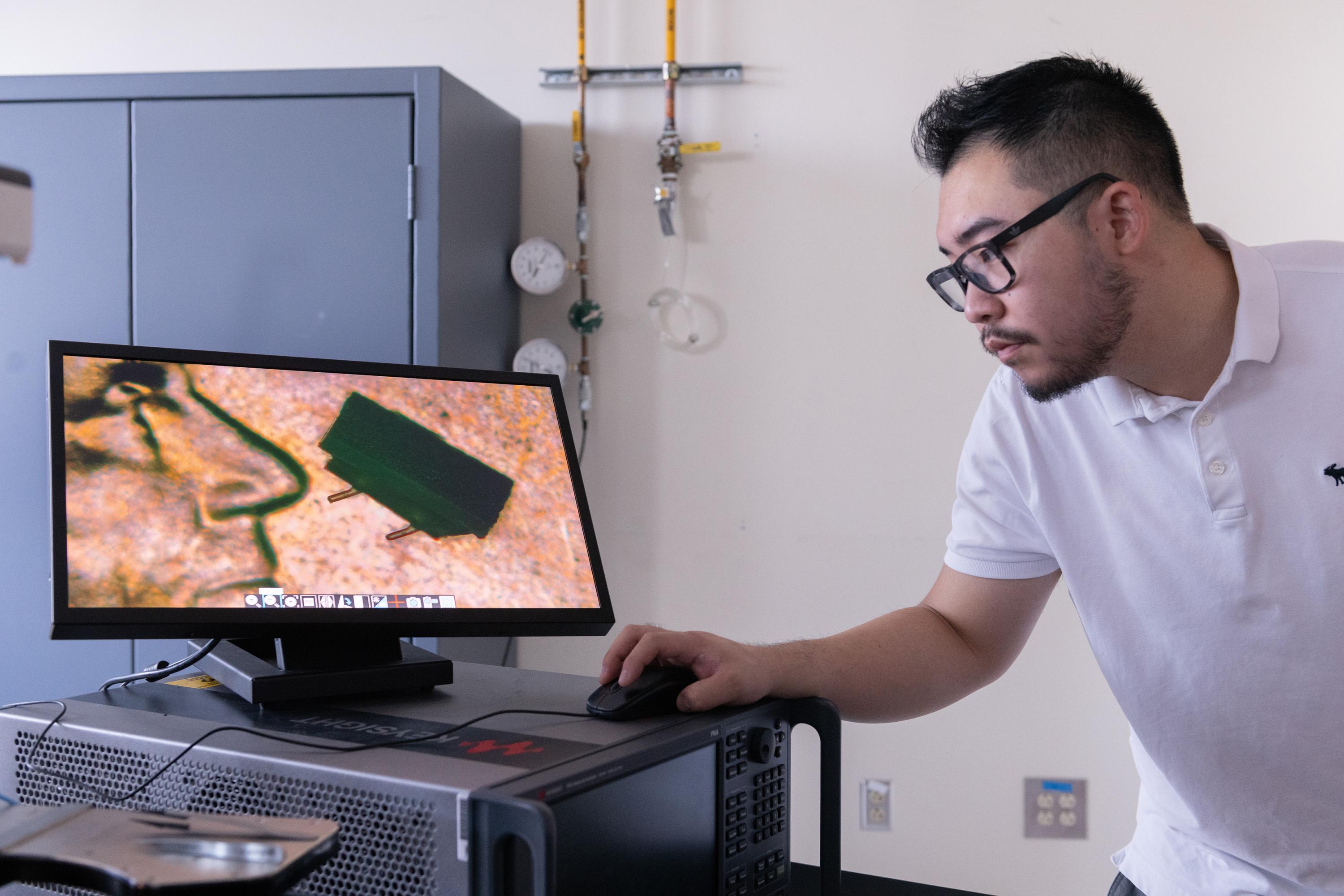 Georgia Tech graduate student Zhijian (Chris) Hao is shown with a microscope image of a micro-bristle-bot on a U.S. penny. (Photo: Allison Carter, Georgia Tech)