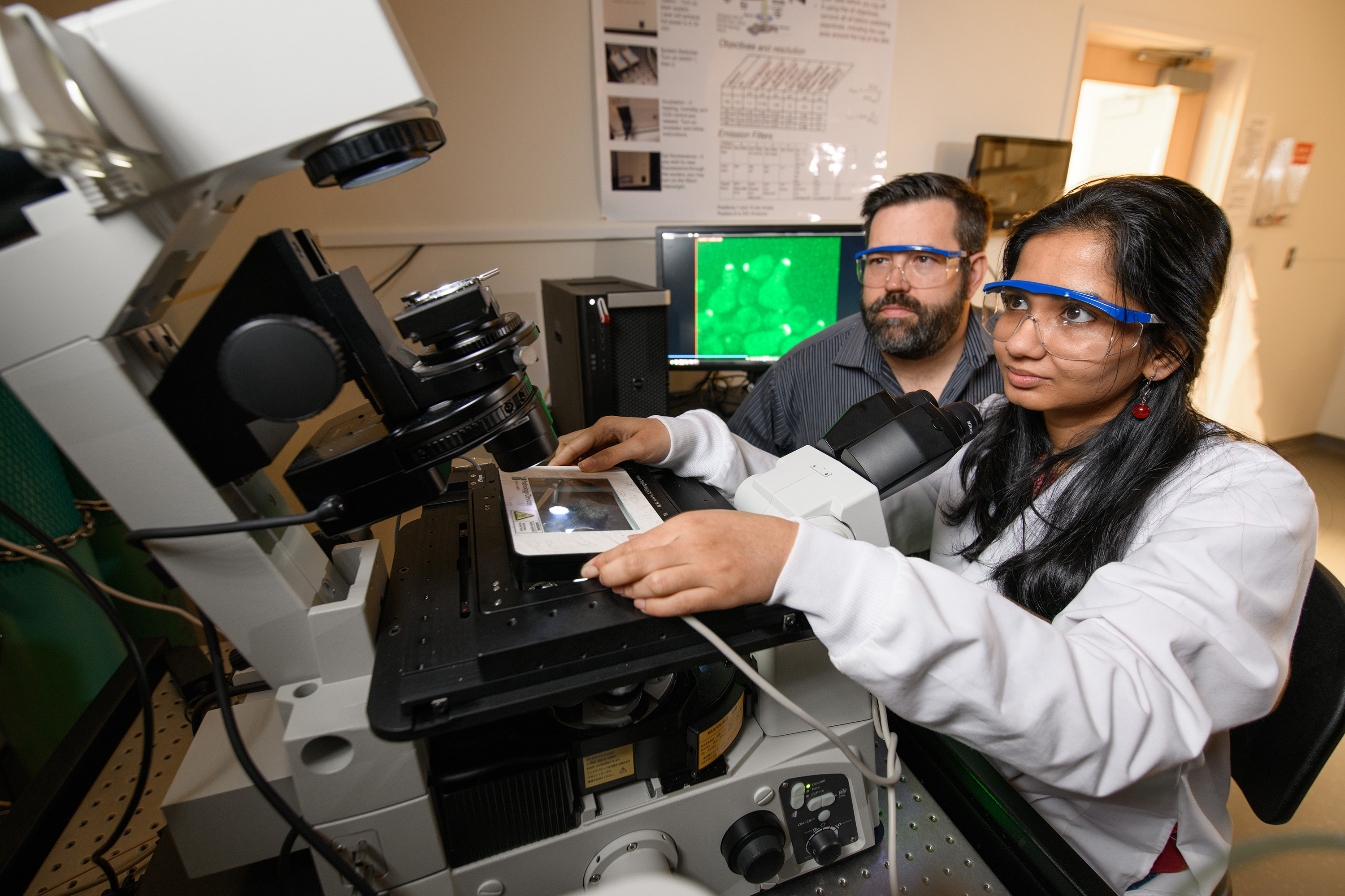 Georgia Tech Associate Professor Matthew Torres and Doctoral Candidate Shilpa Choudhury are shown with images showing cells with a localized green fluorescent protein signal at the membrane. (Credit: Rob Felt, Georgia Tech)