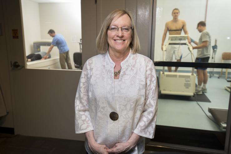 Professor Mindy Millard-Stafford researches in exercise physiology, including studies on how dehydration and exertion can reduce physical and cognitive performance. In the background, a volunteer lies on a device that measures body composition (l.) and another volunteer sweats out fluids under exertion in a heated chamber (r.). Millard-Stafford is Past President of the American College of Sports Medicine. Credit: Georgia Tech / Christopher Moore