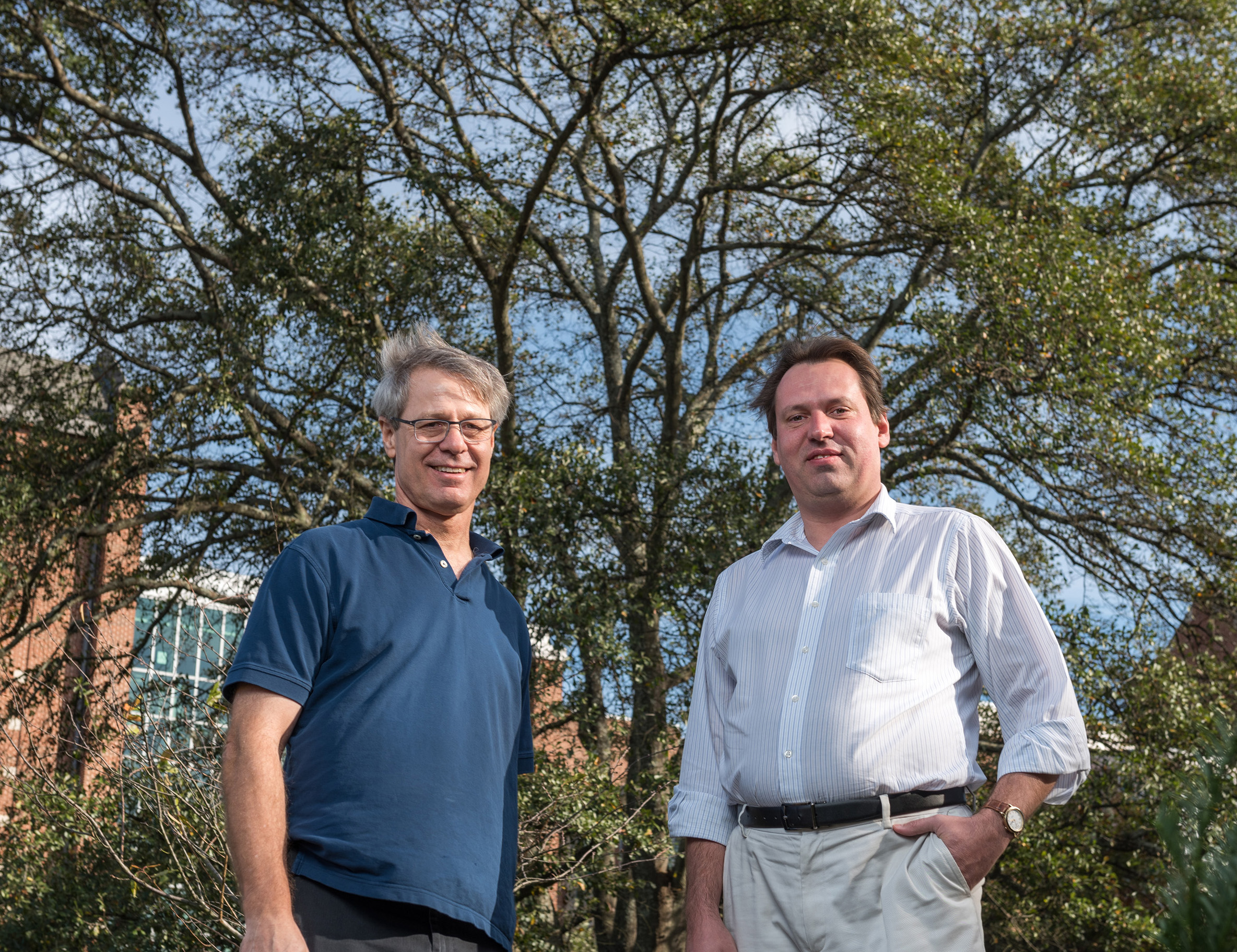 Image shows Georgia Tech Professor Loren Williams (left) and Research Scientist Anton Petrov in front of a large tree that symbolizes the growth and accretion of the ribosome over time. (Credit: Rob Felt, Georgia Tech)