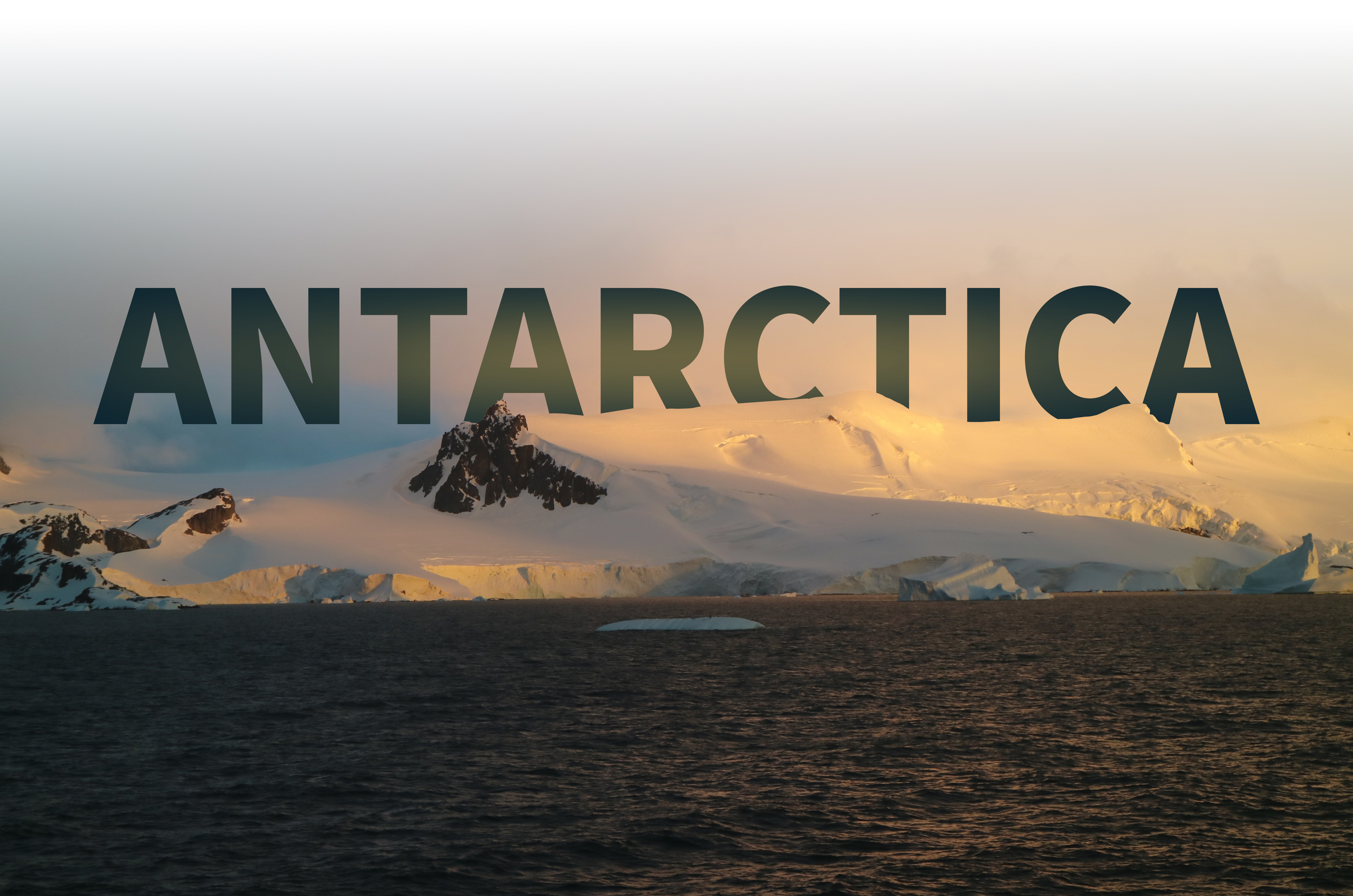 An image of Antarctica at sunset with orange skies on a snowy mountain next to the sea.